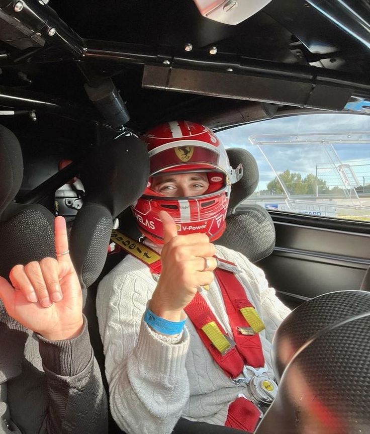 a person in a race car giving the peace sign with both hands and wearing a red helmet