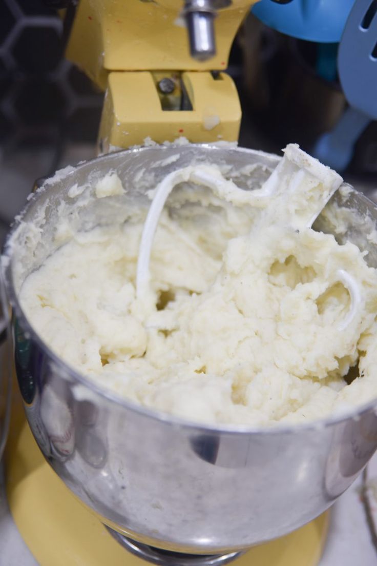 a metal bowl filled with mashed potatoes sitting on top of a yellow stand mixer