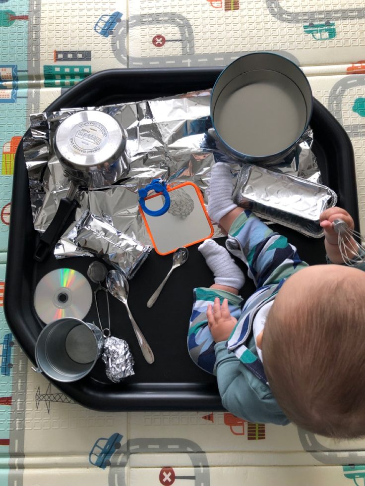 a baby sitting on top of a black tray covered in tin foil and cooking utensils