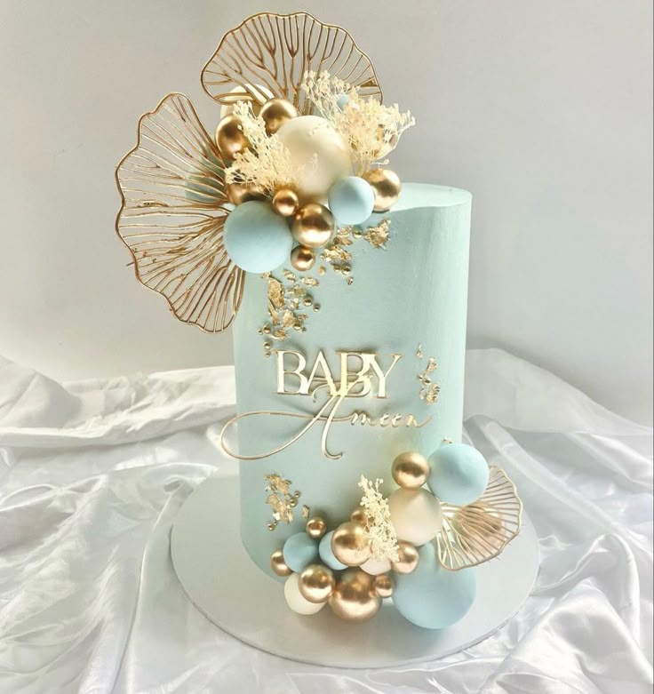 a blue and gold baby shower cake on a white tableclothed surface with golden decorations