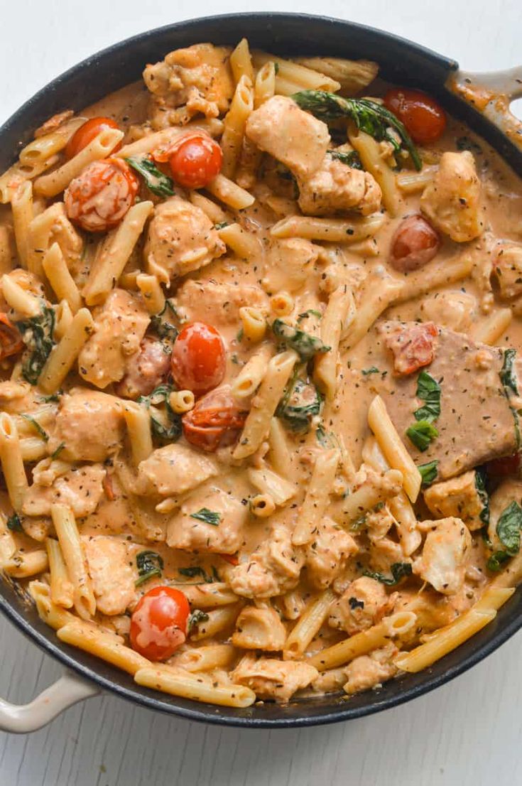 a skillet filled with pasta, chicken and tomatoes