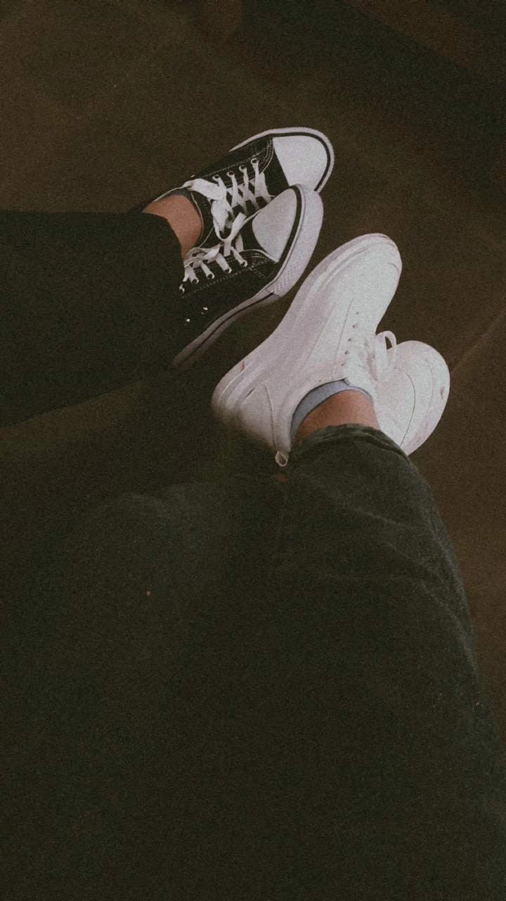 a person wearing white sneakers and black pants sitting on the floor with their legs crossed