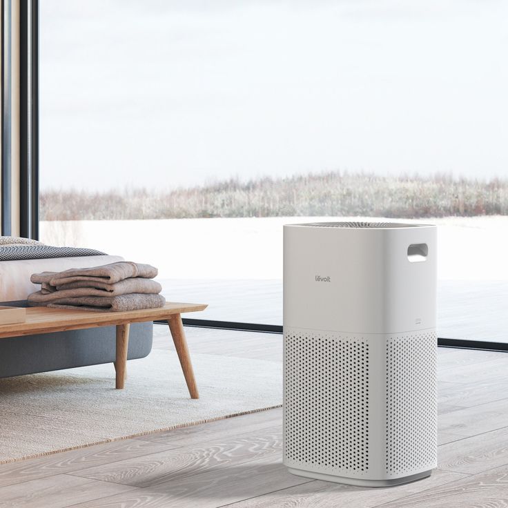 an air purifier sitting in front of a window next to a couch