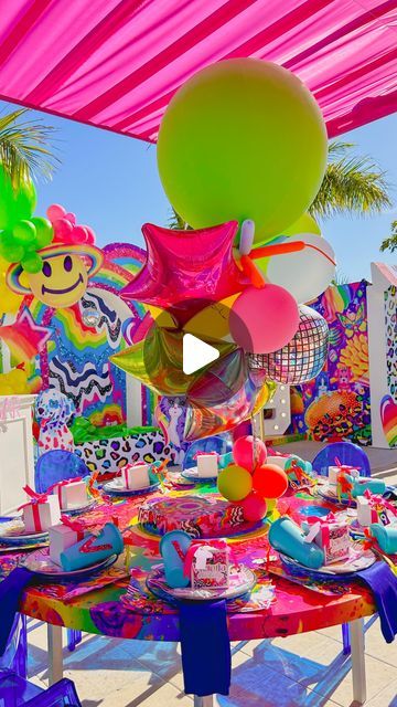 an outdoor party with balloons, plates and cake on a table under a colorful canopy