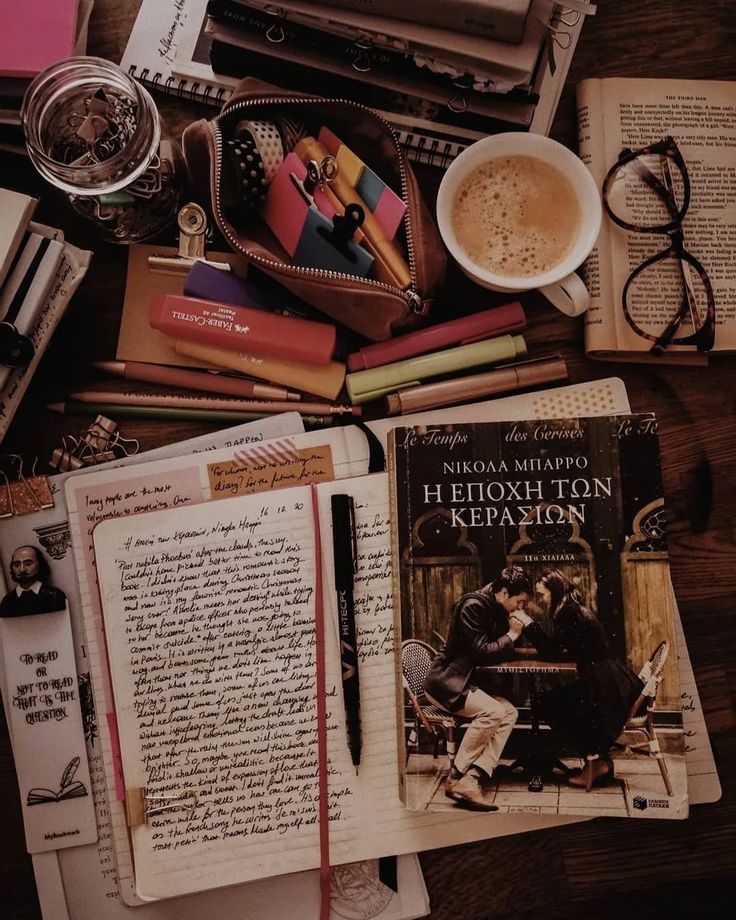 an assortment of books, papers, and other items on a wooden table with a cup of coffee