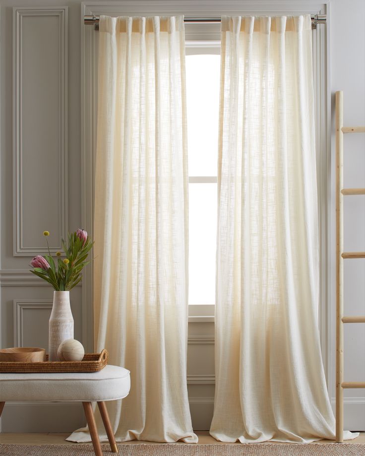 a window with white curtains in front of it and a vase filled with flowers next to the window