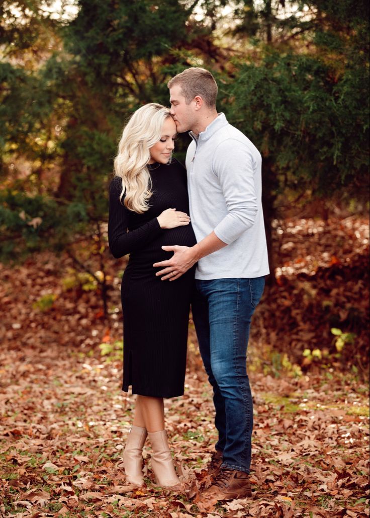 a pregnant couple cuddles while standing in the leaves