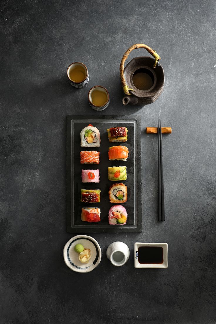 sushi on a tray with chopsticks, sauce and two cups next to it