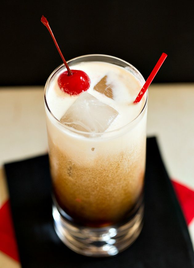 a drink with ice and a cherry garnish on the top is sitting on a black tray