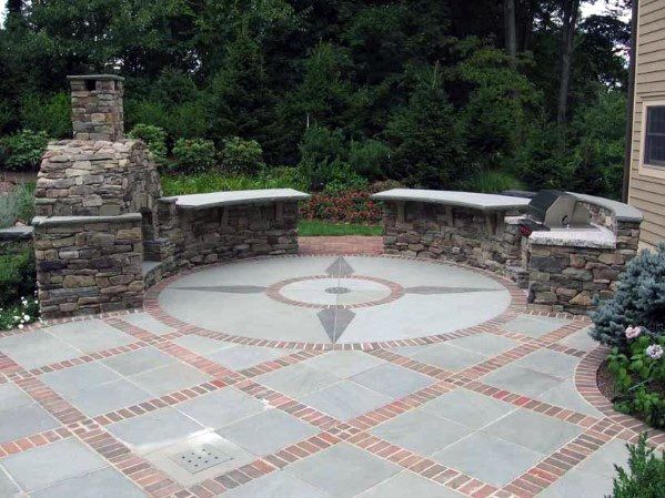 a stone patio with benches and trees in the background