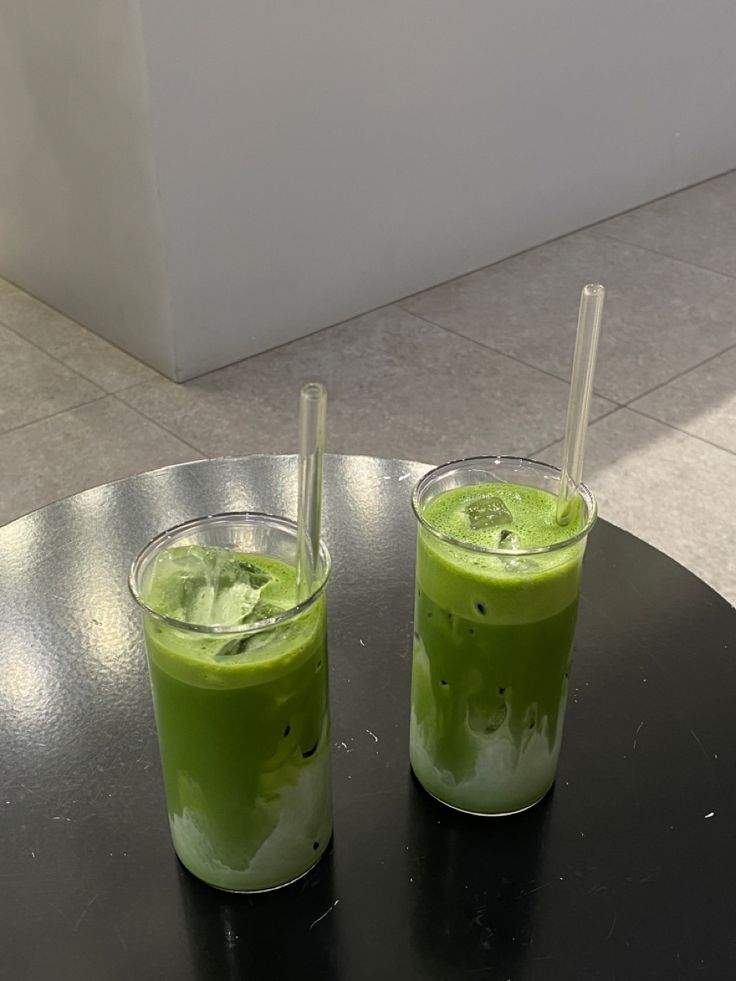 two glasses filled with green liquid sitting on top of a black table next to each other