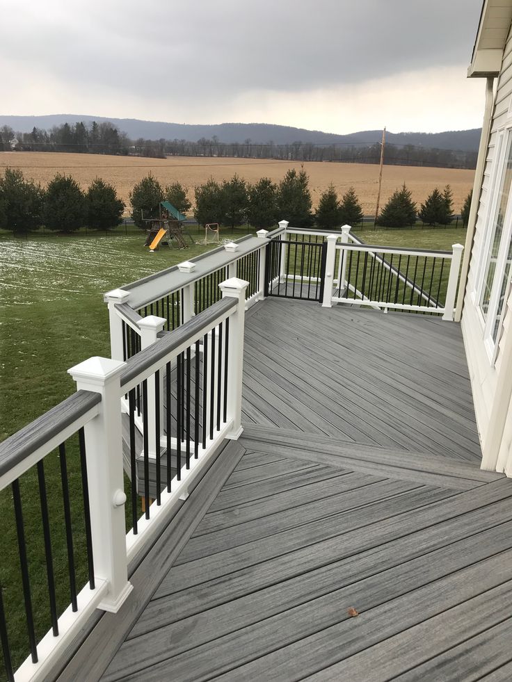 a wooden deck with white railings in front of a large grassy field and trees