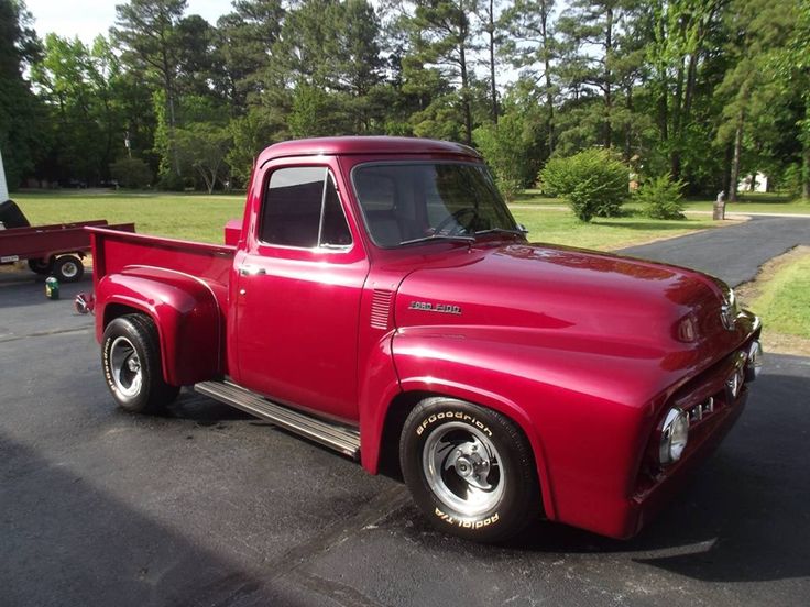 an old red pick up truck parked in a parking lot next to a picnic table