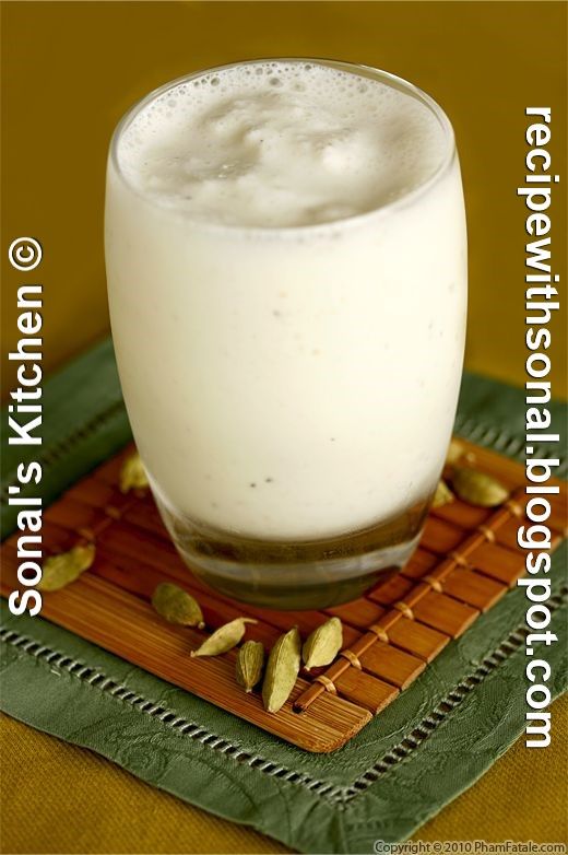 a glass filled with white liquid sitting on top of a wooden table next to a green napkin