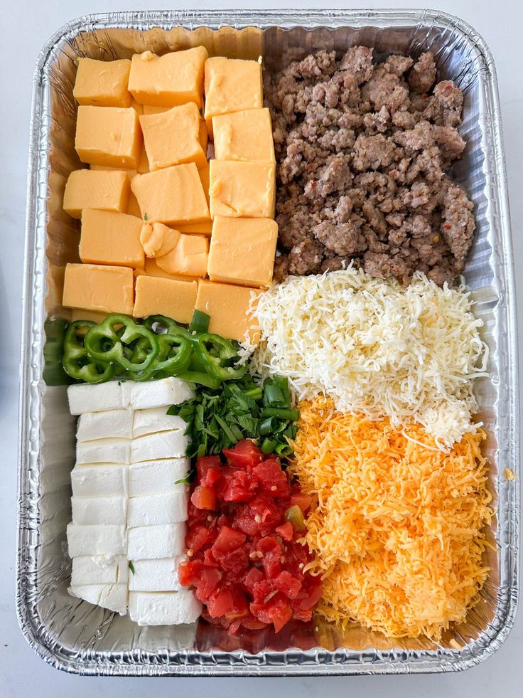 an assortment of cheeses, meat and vegetables in a tin container on a table