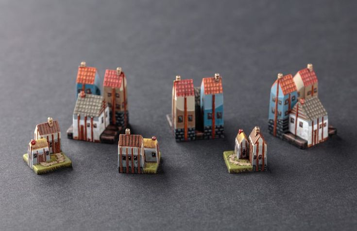 several miniature buildings are shown on a table top with grey background and black surface,