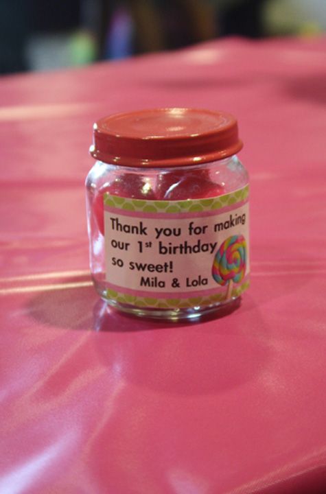 a pink table topped with a jar filled with candy and a label that says thank you for making our birthday so sweet & lolli