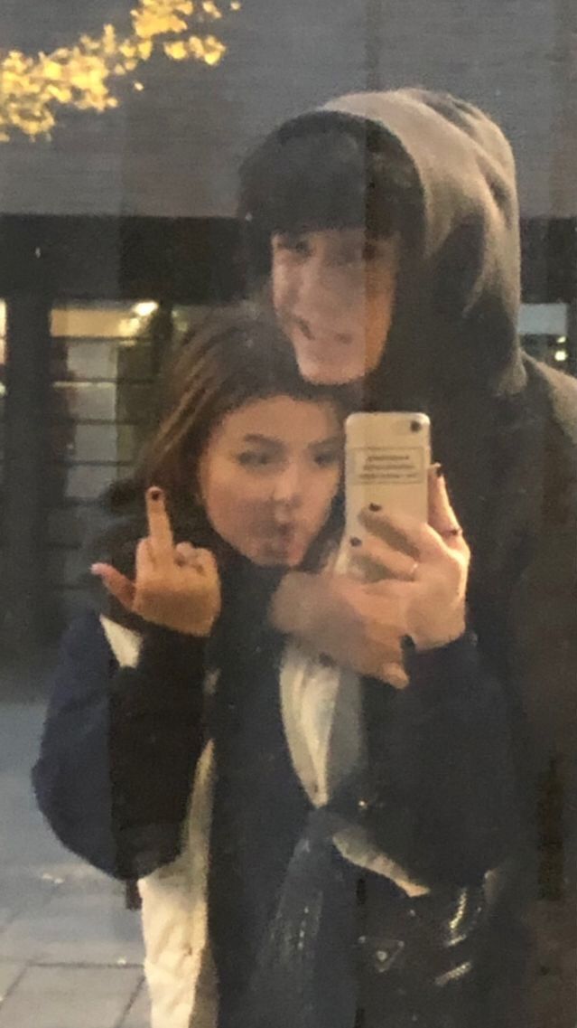 two people taking a selfie in front of a building while holding up their cell phones