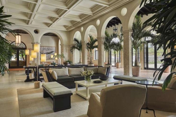 a large living room with couches and chairs in it's center hall, surrounded by palm trees