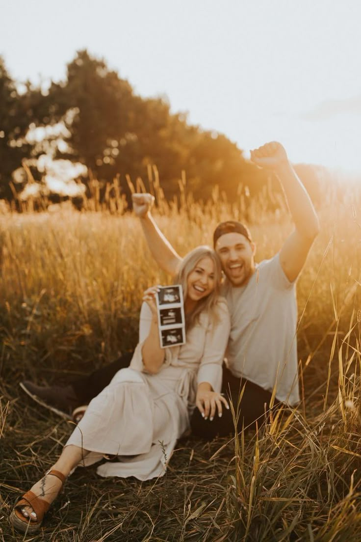 a man and woman sitting on the ground in tall grass with their arms around each other