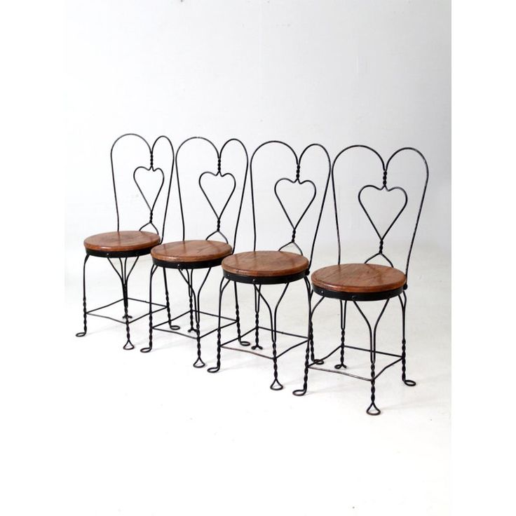 four wrought iron chairs with wooden seats and hearts on the back, set against a white background