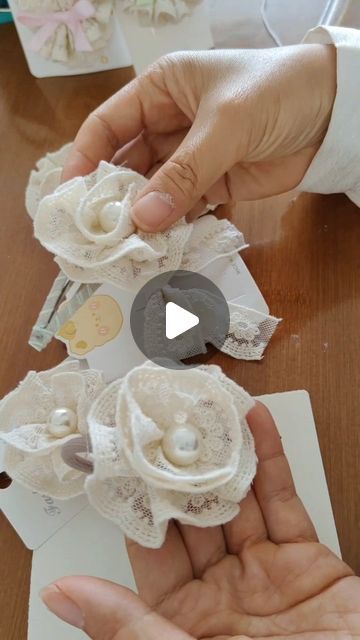 two hands holding small white flowers on top of a table