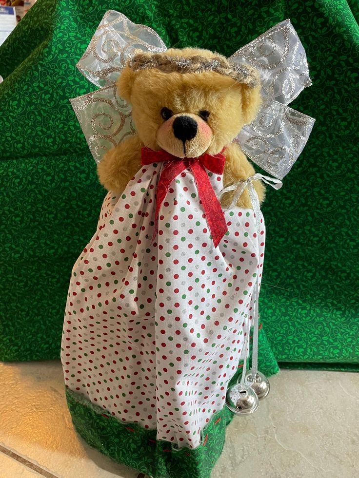 a teddy bear dressed as an angel sitting in a gift bag with bells on it