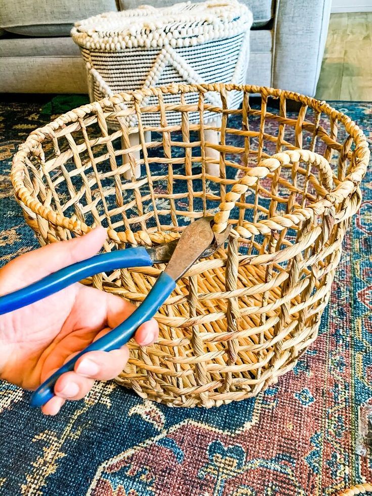 a person holding scissors in front of a basket on the floor next to a couch