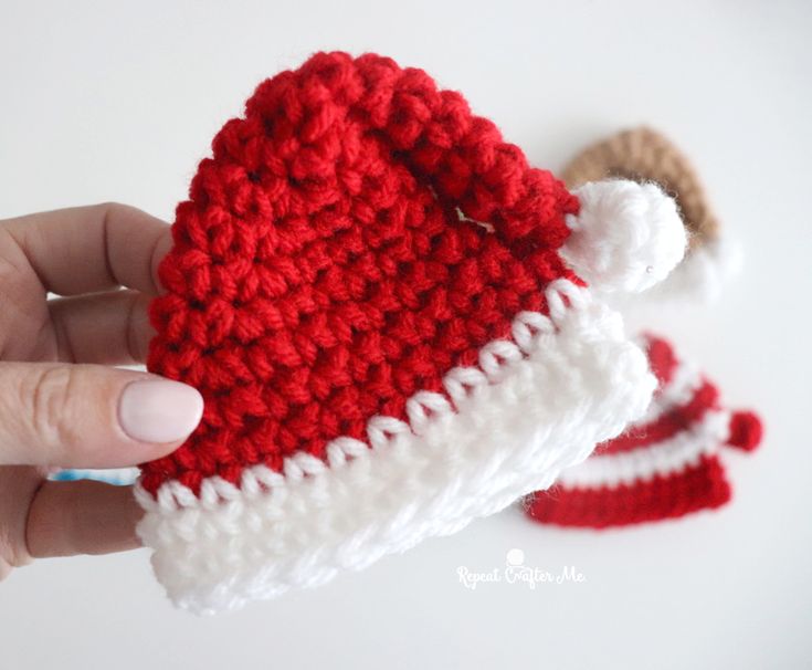 a hand holding a crocheted santa hat with two small hats on top of it