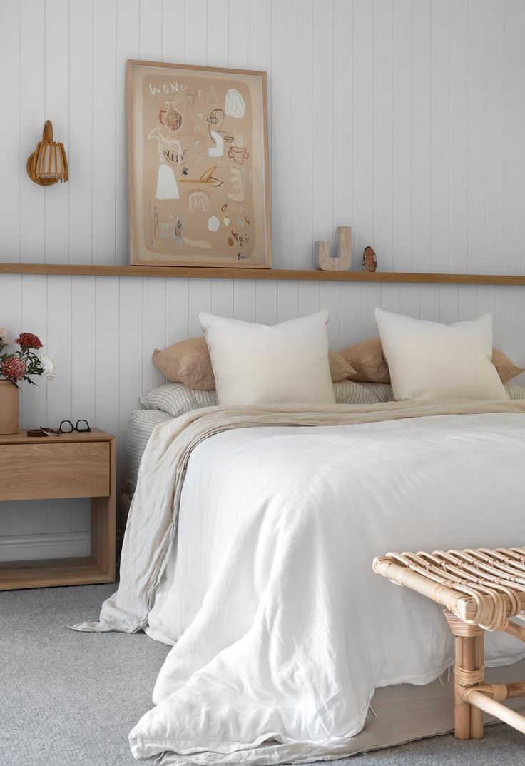 a bed with white linens and pillows in a small room next to a wooden bench