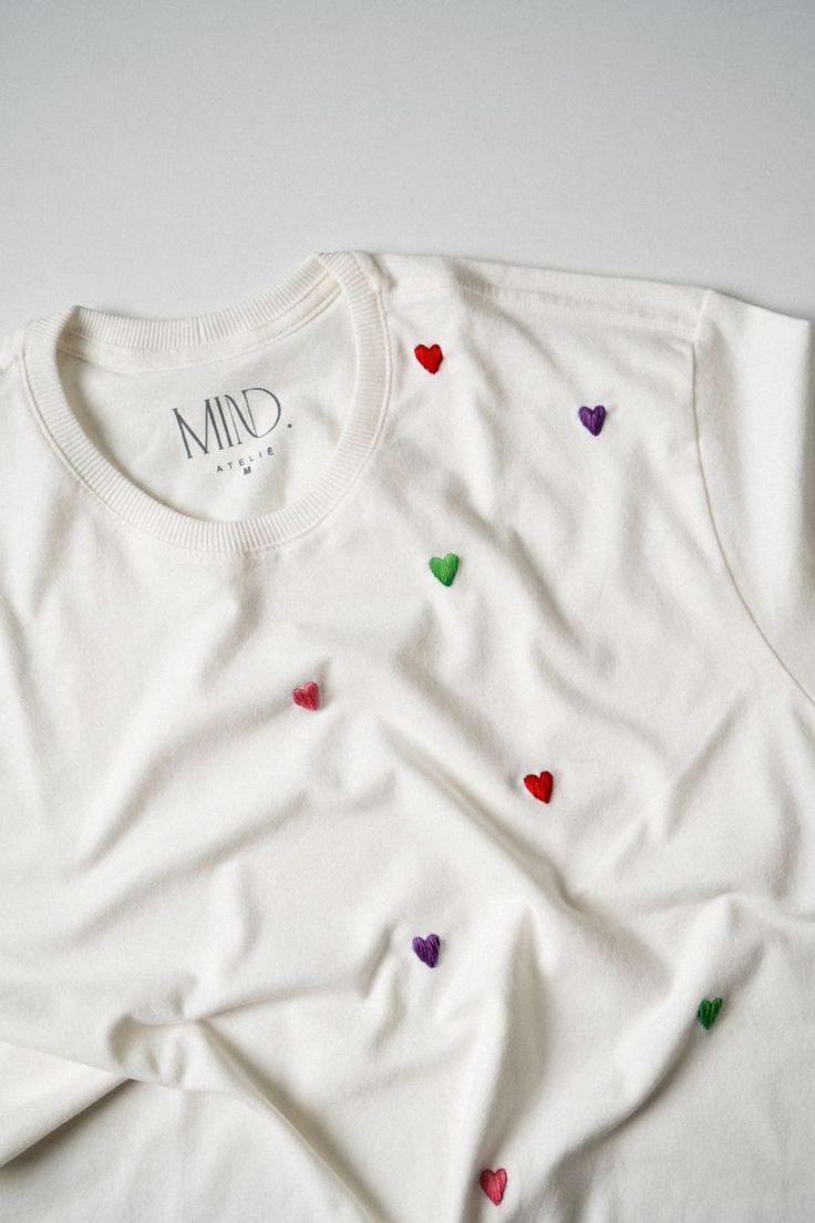 a white t - shirt with colorful hearts on the front and back, sitting on top of a table