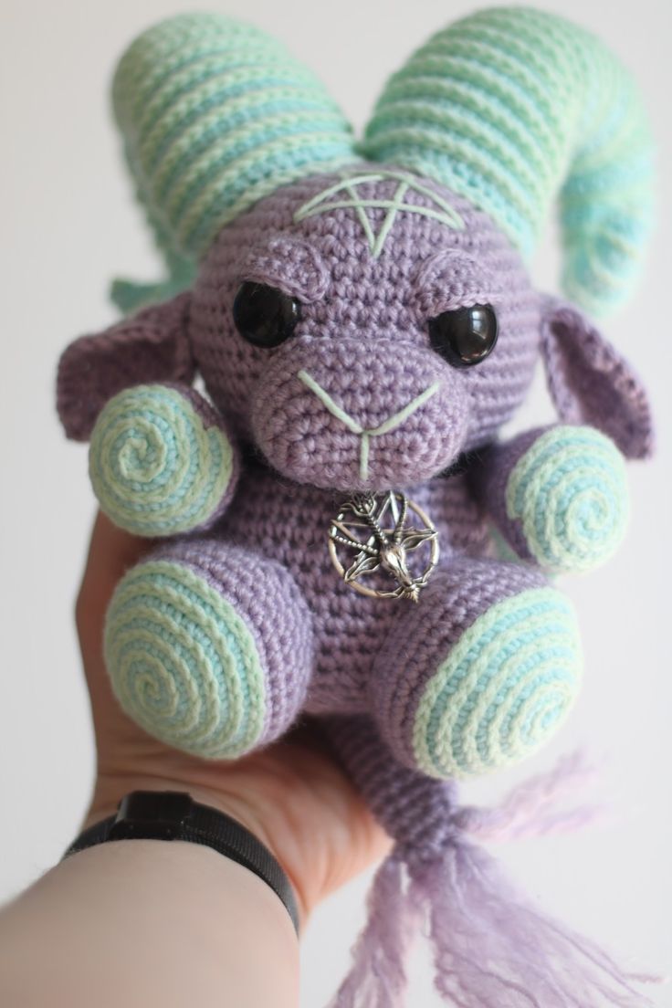 a hand holding a small crocheted purple and green stuffed animal with black eyes