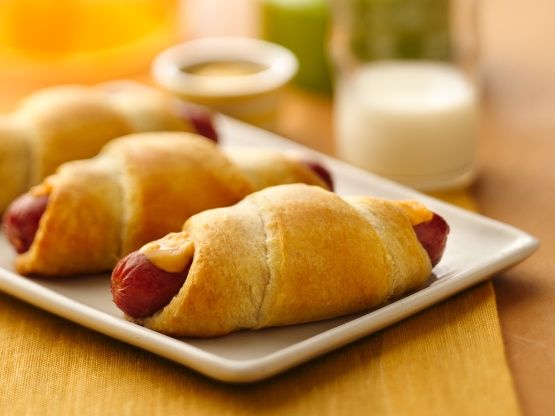 two hot dogs wrapped in bread on a white plate with milk and oranges behind them