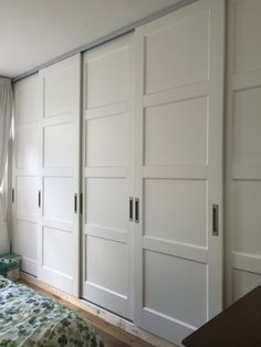 a bedroom with white closet doors and green bedspread on the bed, in front of a window