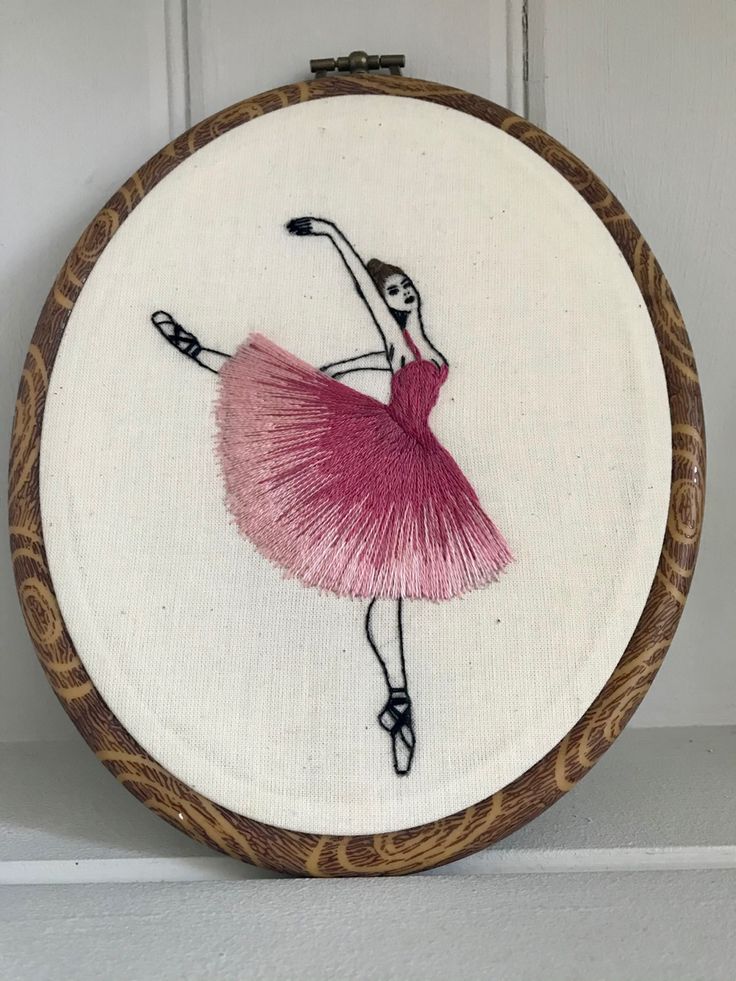 a hand embroidered ballerina in pink on a white background with wooden hoop hanging from the wall