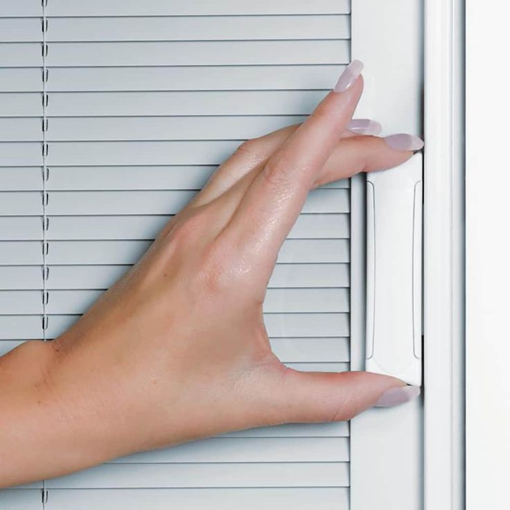 a person's hand is holding on to a closed door with blinds behind them