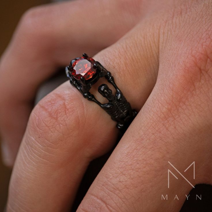 a close up of a person's hand wearing a black ring with red stones