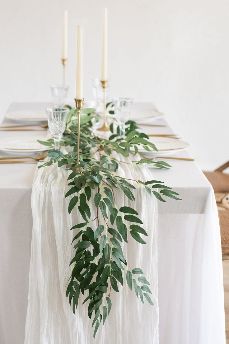 the table is set with white linens and greenery