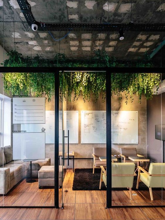 an office with glass walls and plants growing on the ceiling, along with wooden flooring