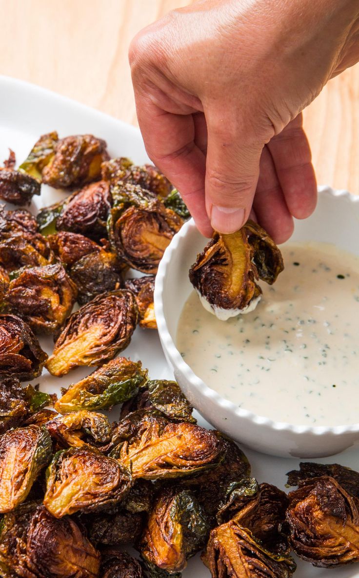 a person dipping something in a small bowl on top of some roasted brussel sprouts