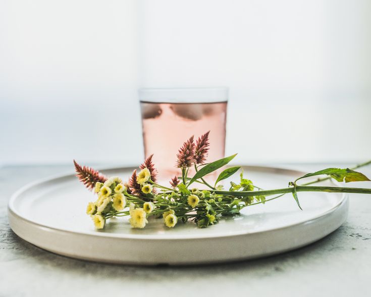 some flowers are sitting on a plate next to a glass with water and tea in it