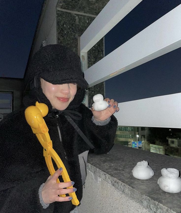 a woman in a black coat is holding a yellow blow dryer and some white balls