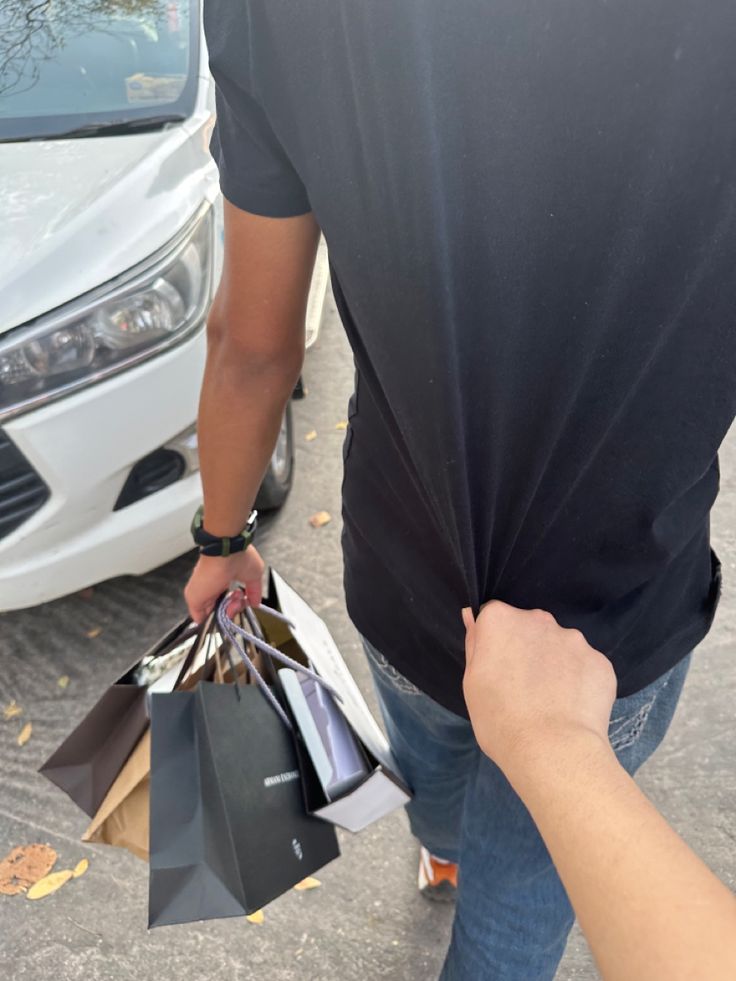 a man is holding shopping bags in his hand while standing next to a white car