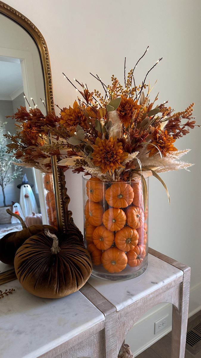 a glass vase filled with lots of oranges on top of a table next to a mirror