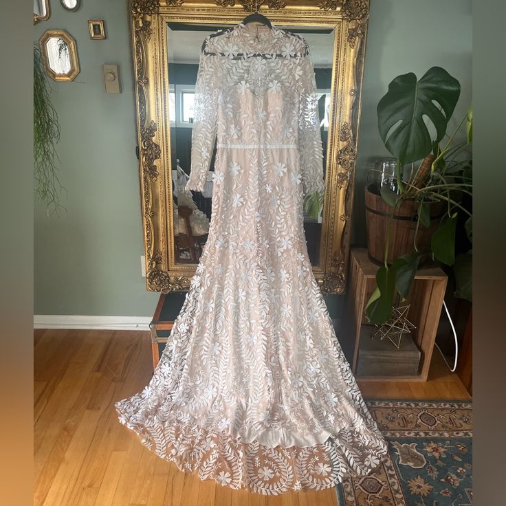 a white wedding dress hanging in front of a mirror on a wooden floor next to a potted plant