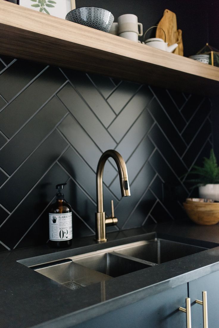 a kitchen with black counter tops and gold faucet, brass sink, and open shelving