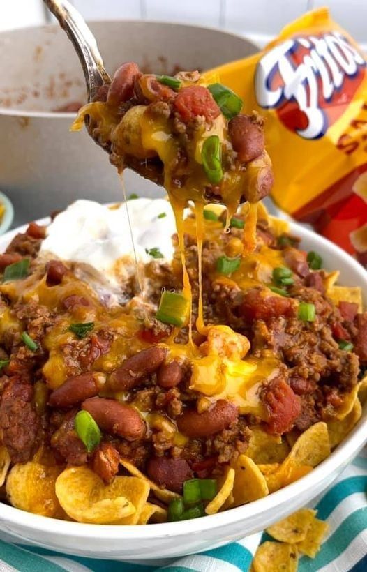 a bowl filled with chili cheese and tortilla chips, topped with sour cream