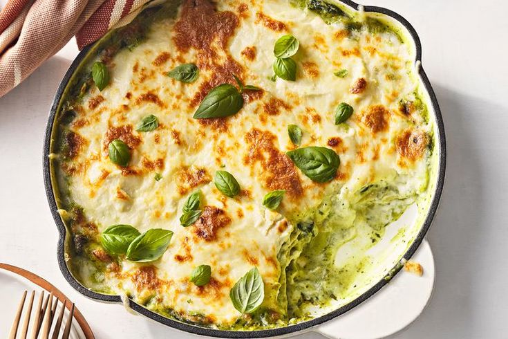 a casserole dish with spinach, cheese and sauce in it on a white table