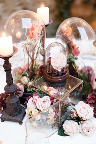 a table topped with two glass globes filled with flowers and greenery next to candles