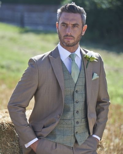 a man in a suit standing next to hay bales wearing a boutonniere